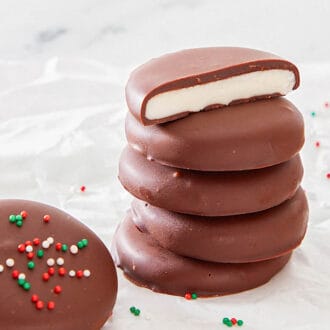 A stack of peppermint patties, the top one cut in half, surrounded by more peppermint patties with sprinkles on top.
