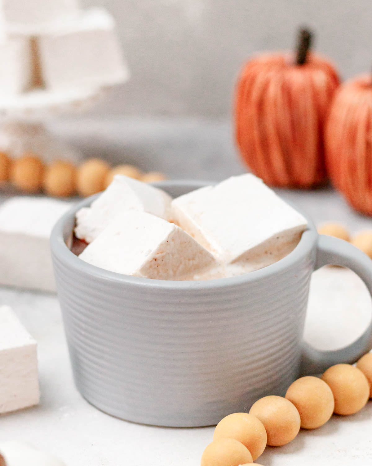 angled image of 3 Pumpkin Spice Marshmallows floating in hot cocoa served in a light gray mug