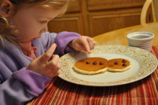 little girl putting chocolate chip snowman pancakes