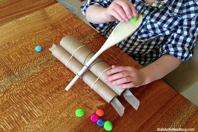 Young man shoots pom poms from a catapult he made using spoons, rubber bands and cardboard tubes