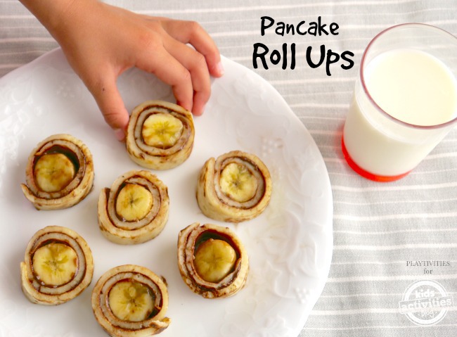 Child picks up a pancake roll with the text: pancake rolls on a plate with a glass of milk