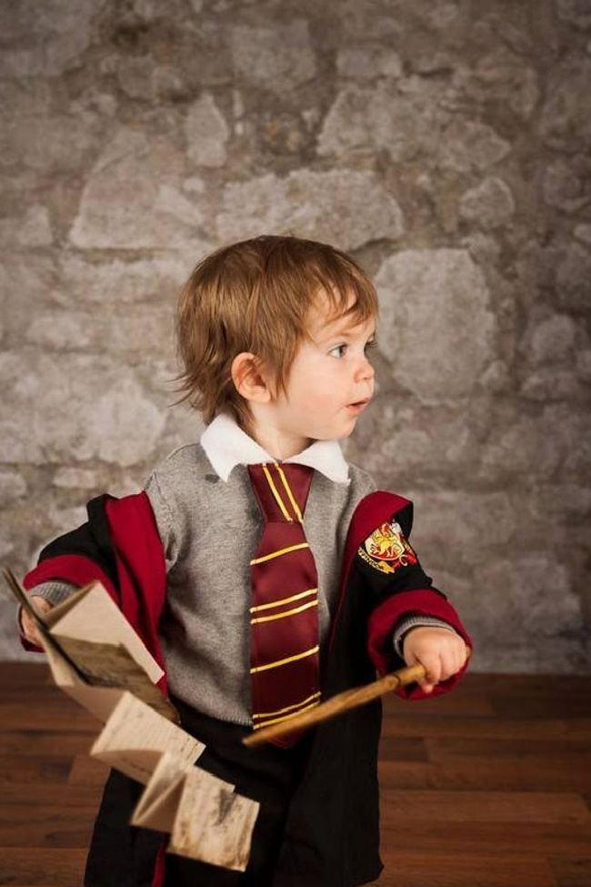 Harry Potter toddler costume based on a young boy holding a wand and the Map of Maurader in front of a stone wall.