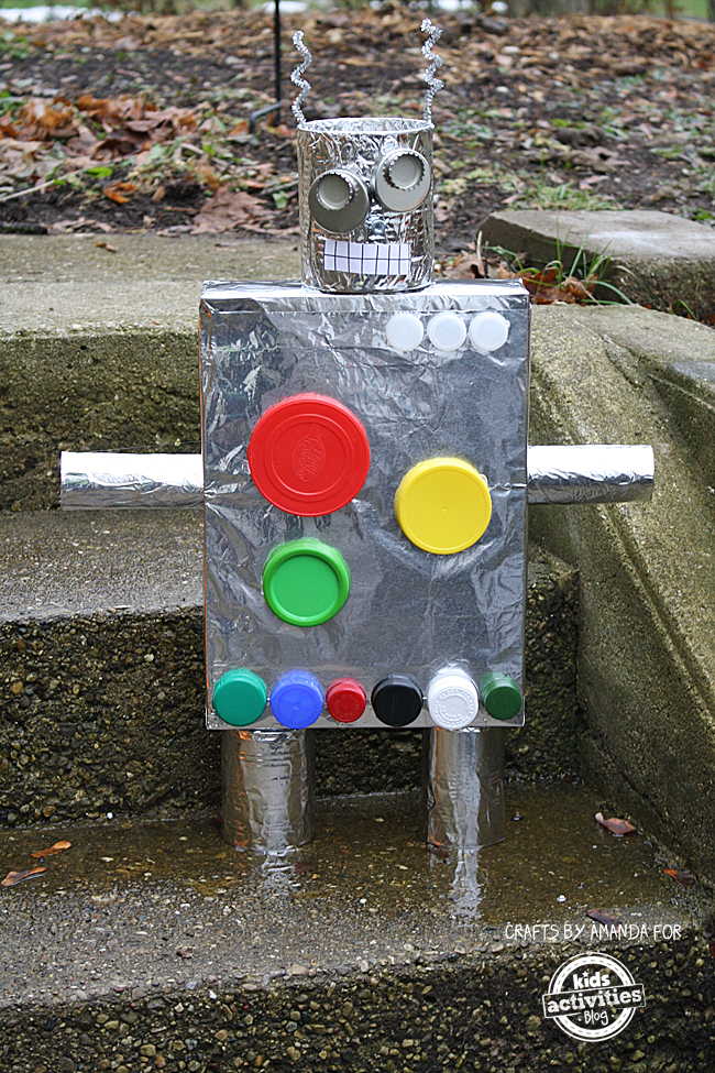 Learn how to make a robot with Recycled Crafts: Cereal Box Robots - Robots made of tinfoil, colorful lids, caps, paper, tape and cans and pipe cleaners on a stone staircase