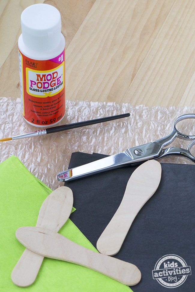 Supplies needed to make this firefly craft kit - mod podge, black tissue paper and green tissue paper, brush and wooden spoon.