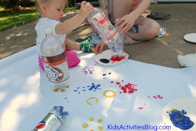 Step 5 - Paint flowers with water bottles - Put paint on paper plate and dip water bottle in it - Little girl stamps paint and water bottle on big piece of paper to make flowers - blue flowers, yellow flowers, red flowers