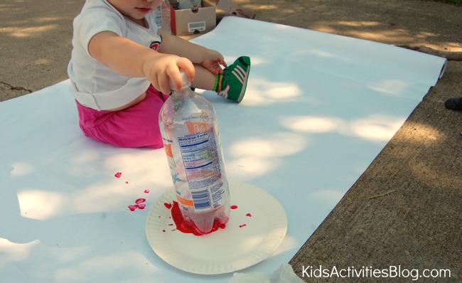 Step 4 - Paint flowers with water bottles - Put paint on paper plate and dip water bottle in it - little girl stamps paint and water bottle on big piece of paper to make flowers