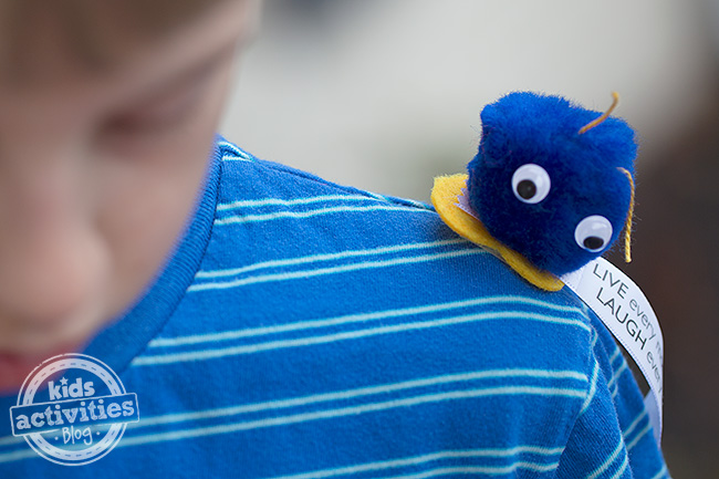 Boy and pom pom critter sitting on his shoulder - blue pom pom friend with googly eyes and bow with positive message - kids activity blog