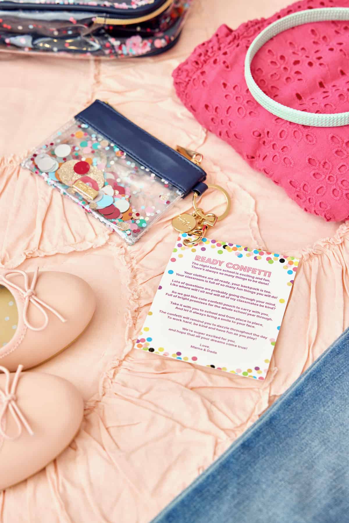 A small glittery keychain pouch, a pair of pink children's ballet flats and a bright pink children's eyelet-toe shirt on a light pink ruffled bedspread.