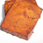 Two blocks of smoked tofu that have been turned a deep red by the barbecue sauce sit on a white serving plate.
