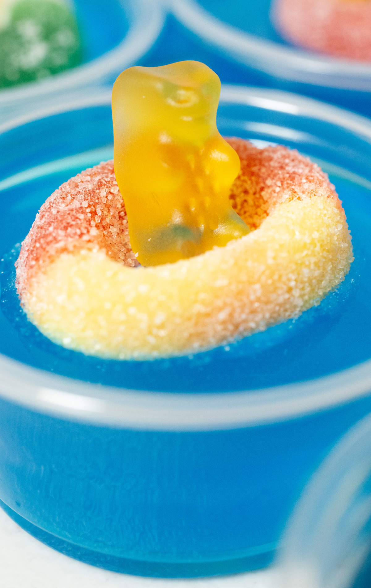A single pool party jello shots with blue gelatin and a peach gummy ring with yellow gummy bear floating on top.