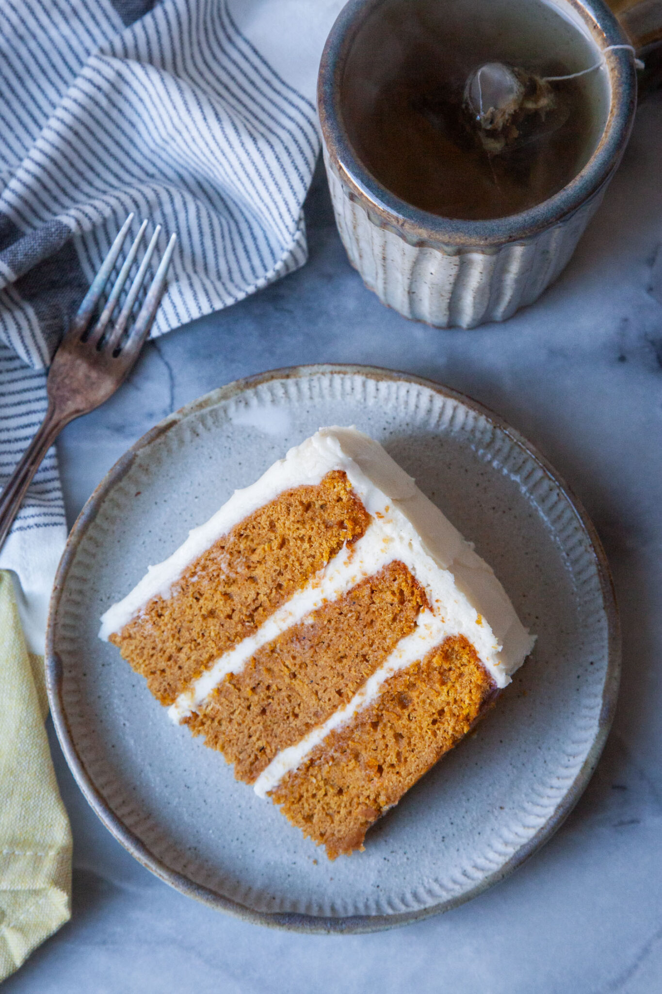 A slice of pumpkin layer cake on a plate, with a mug of tea next to it. 