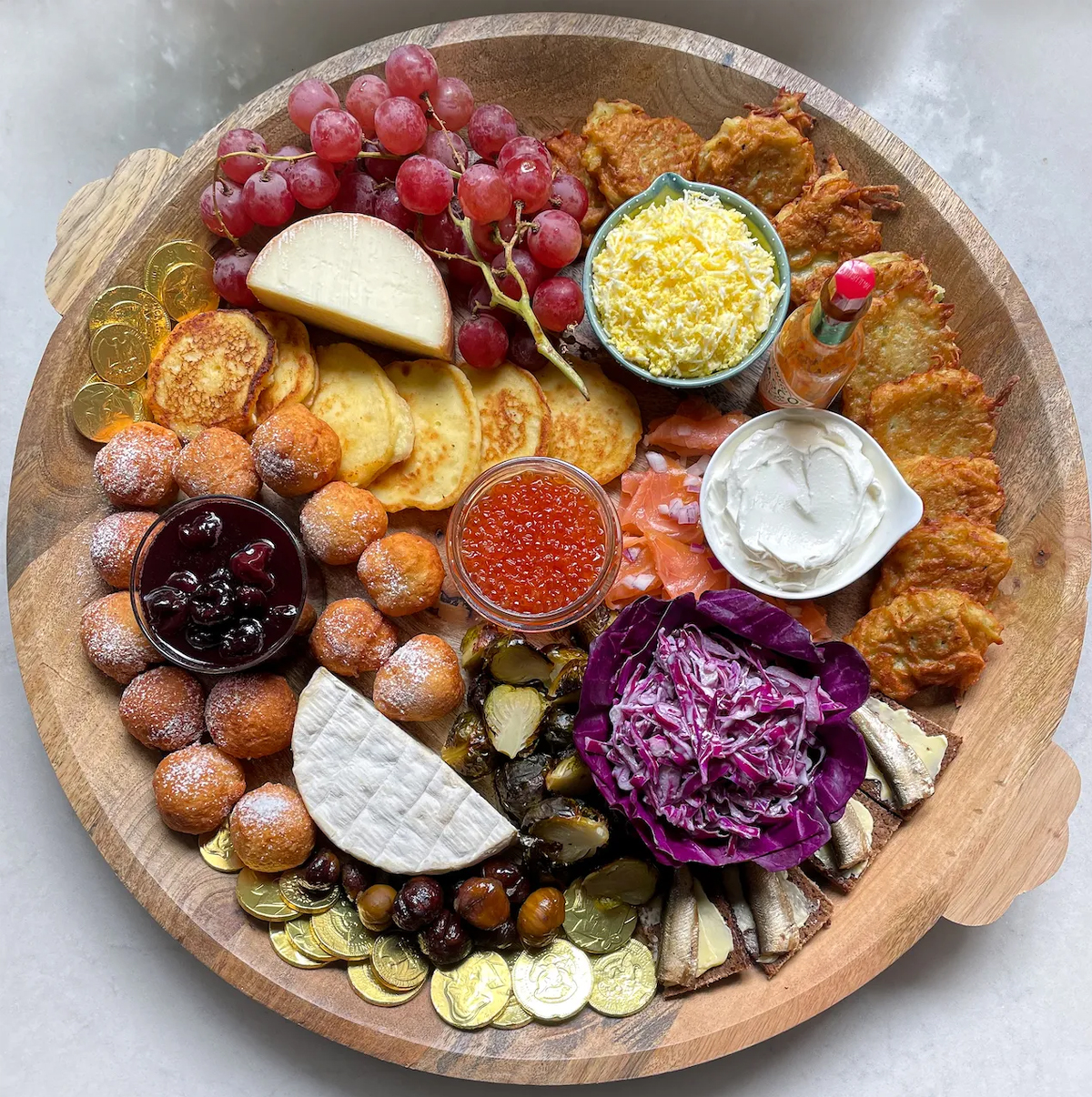 a wooden dish from Verde guttmans with latkes, golden chocolate coins, grapes, cheese, dips and more. 