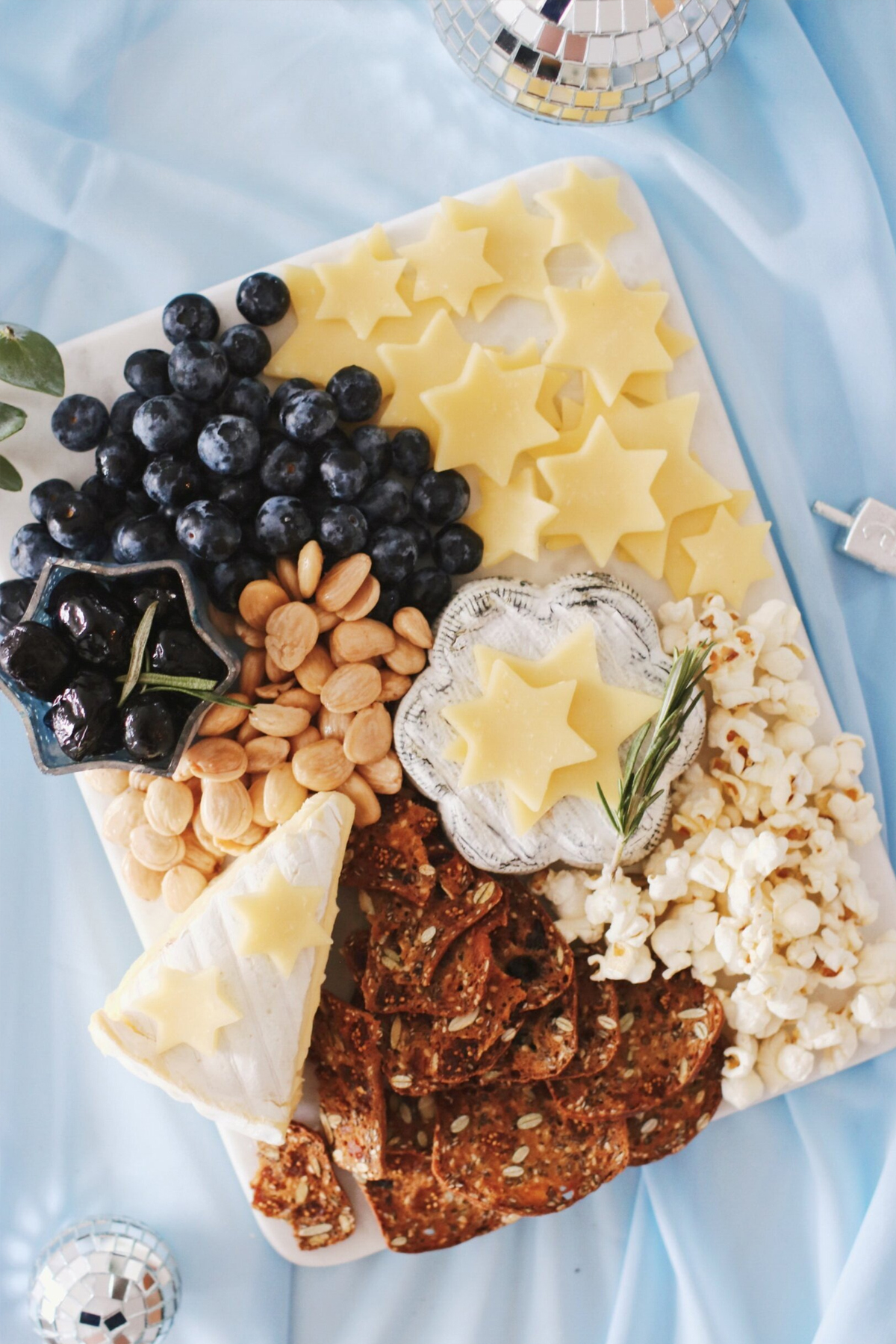 Star of David sliced cheese, brie blueberries, crackers, and popcorn are all on this Hanukkah charcuterie board recipe from Rebekah Lewin