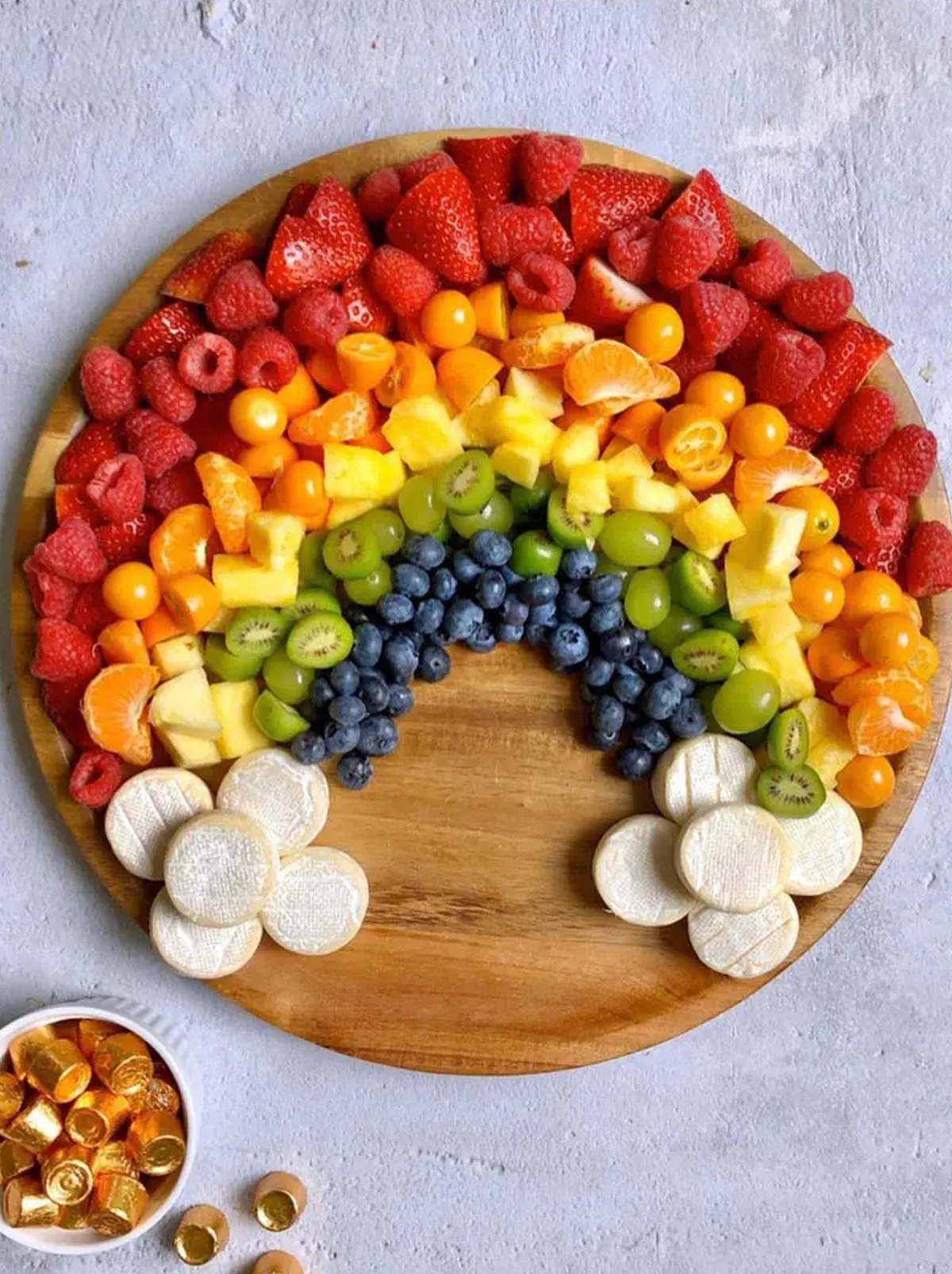 One of the easiest rainbow charcuterie board ideas with colorful fruit and brie cheese as clouds from aint too proud to meg.