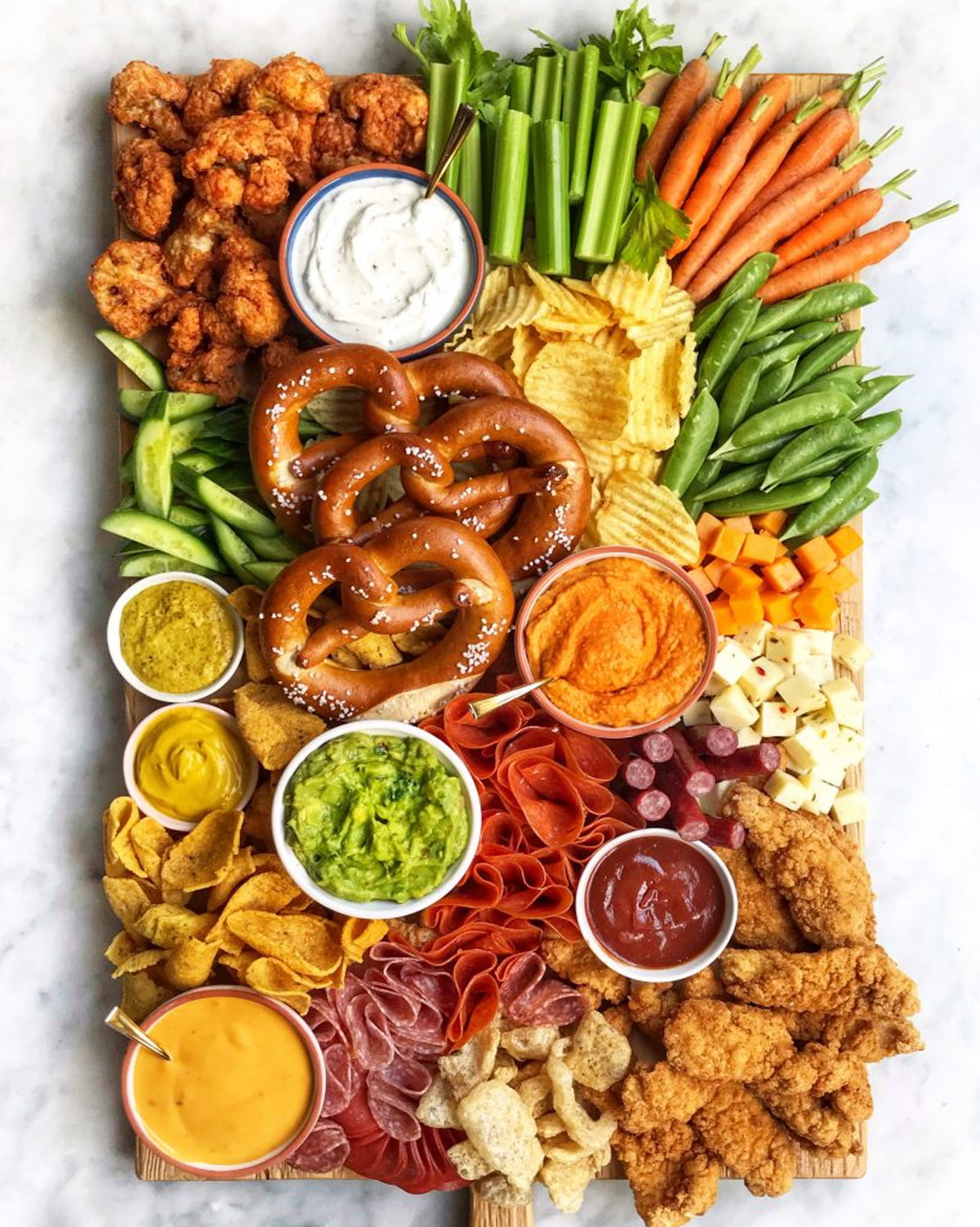 Dips, chips, cheese, crackers, meat, pretzels, and veggies are included on The Delicious Life charcuterie board.