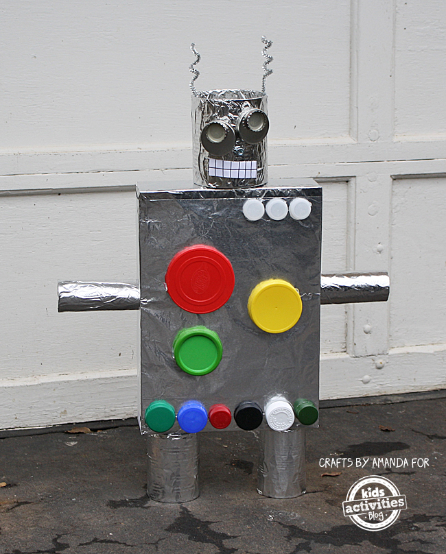 Robots made from tinfoil, colorful lids, caps, paper, tape and cans and pipe cleaners in front of a garage door - how to make a robot - Recycled Crafts: Cereal Box Robots