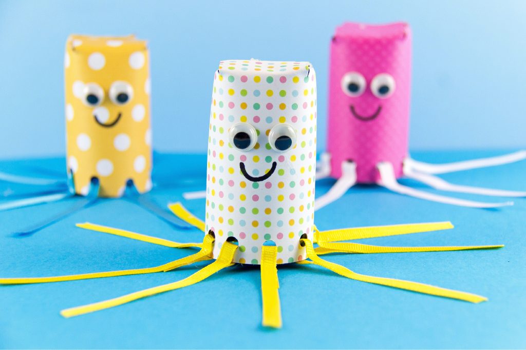 Toilet paper octopus craft wrapped in white and yellow and pink paper with polka dots and ribbon tentacles.